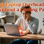 "Thoughtful man in gray sweater with hand on face looking at laptop with orange-red glow from keyboard area on wooden desk with white lamp and monstera plant. Text overlay reads 'Stop Laptop Overheating Without a Cooling Pad'"